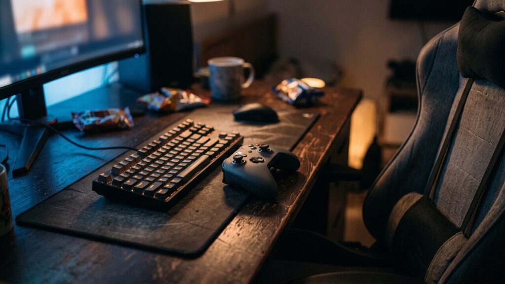 Een game-opstelling in een donkere kamer met toetsenbord en controller, het scherm werpt licht op het bureau.