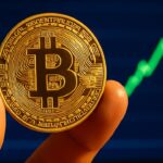Fysieke Bitcoin-munt voor een scherm met een stijgende groene koersgrafiek