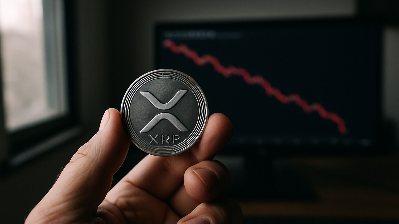 Een hand houdt een fysieke XRP-munt vast voor een scherm met een dalende rode koersgrafiek