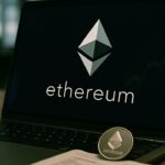 Ethereum-logo op een laptopscherm met een fysieke ETH-munt op een bureau in een bedrijfskantoor