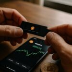 Handen houden een hardware-wallet vast naast een smartphone met een beurs-app, na het Coldcard-lek