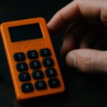 Een oranje Coldcard hardware wallet op een donker bureau naast een dobbelsteen, symbool voor willekeur en sleutelgeneratie