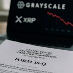 Officieel SEC-document op een bureau met op de achtergrond een laptop die een dalende rode XRP-grafiek en het Grayscale-logo toont
