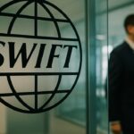 Het SWIFT-logo op een glazen wand in een modern bankkantoor met een medewerker op de achtergrond