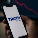 Smartphone met de Truth Social-app en op de achtergrond een rode dalende koersgrafiek op een scherm