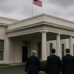 Bestuurders in pak lopen naar de ingang van het Witte Huis in Washington onder een bewolkte hemel.
