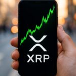 Een hand houdt een smartphone vast met een stijgende groene XRP-koersgrafiek en het XRP-logo op het scherm