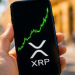 Smartphone toont een stijgende groene XRP koersgrafiek met het XRP-logo in beeld