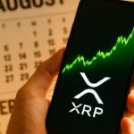 Smartphone toont een stijgende groene XRP koersgrafiek, met een kalender die van augustus naar september wisselt op de achtergrond.