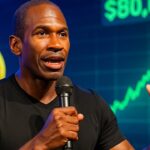 Arthur Hayes spreekt op een podium voor een scherm met een stijgende Bitcoin koers boven 80.000 dollar