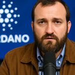 Charles Hoskinson, oprichter van Cardano, spreekt in een microfoon met het Cardano-logo op de achtergrond