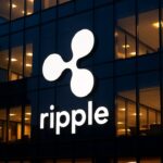 Gevel met groot verlicht Ripple-logo bij schemering