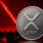 Fysieke XRP munt met logo voor een scherm met een dalende rode koersgrafiek