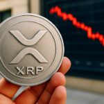 Fysieke XRP-munt met logo voor een scherm met een dalende rode koersgrafiek