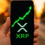 Smartphone toont een groene XRP koersgrafiek met het XRP-logo, buiten op straat