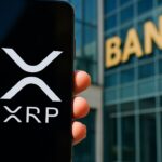 Smartphone met het XRP-logo voor de gevel van een bankgebouw in helder daglicht