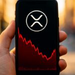 Smartphone toont een XRP-koersgrafiek met het XRP-logo, waar de koers laag staat maar begint op te veren
