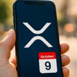 Smartphone met het XRP-logo en een kalender die 9 oktober aanwijst, in een hand op straat