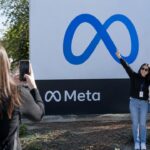 Groot bord met het Meta-logo bij het hoofdkantoor in Menlo Park, met bezoekers die foto's maken