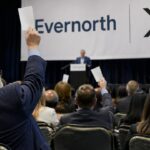 Aandeelhoudersvergadering met een groot Evernorth- en XRP-spandoek op het podium en aandeelhouders die stemkaarten omhoog steken