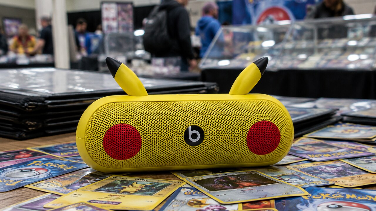 Gele Beats Pill-speaker in Pikachu-stijl met Beats-logo op een stapel Pokémonkaarten op een verzamelbeurs