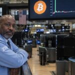 Oudere beurshandelaar leunt op een reling op een bijna lege beursvloer onder een scherm met het Bitcoin-symbool en een afgevlakte grafiek van fondsstromen