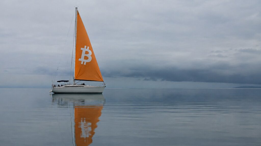 Zeilboot met oranje zeil en Bitcoin-logo ligt stil op een spiegelgladde zee, met donkere wolken aan de horizon