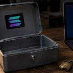 Lege geldkist met Solana-logo naast een kapot hangslot en een laptop met een rode beveiligingswaarschuwing