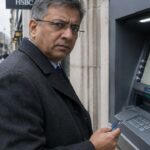 Man met bankpas kijkt gefrustreerd bij een geldautomaat van een Britse bank in Londen, met een rood kruis op het scherm