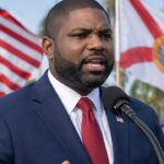 Congreslid Byron Donalds spreekt op een campagnebijeenkomst in Florida, met de Amerikaanse en Floridiaanse vlag en palmbomen op de achtergrond