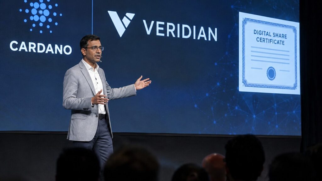 Spreker op een podium van een blockchainconferentie voor een groot scherm met het Cardano-logo en de naam Veridian