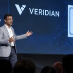 Spreker op een podium van een blockchainconferentie voor een groot scherm met het Cardano-logo en de naam Veridian