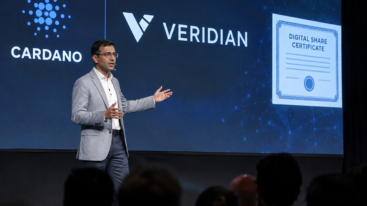 Spreker op een podium van een blockchainconferentie voor een groot scherm met het Cardano-logo en de naam Veridian