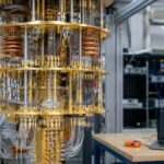 Gouden koelsysteem van een quantumcomputer in een onderzoekslab, met op de achtergrond een laptop met het Bitcoin-logo