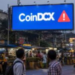 Groot reclamebord met het CoinDCX-logo en een rode waarschuwing boven een drukke straat in Mumbai in de schemering