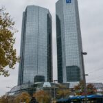 De glazen torens van het hoofdkantoor van Deutsche Bank in Frankfurt met het blauwe logo, gezien vanaf straatniveau