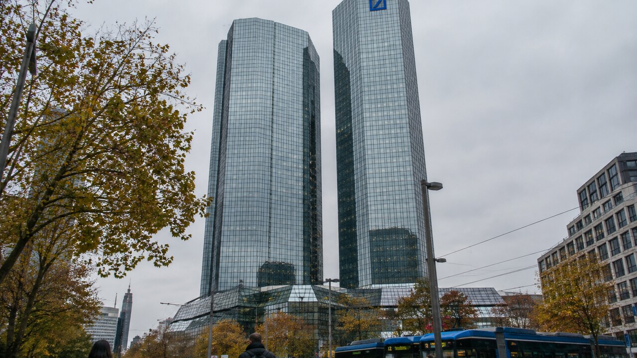 De glazen torens van het hoofdkantoor van Deutsche Bank in Frankfurt met het blauwe logo, gezien vanaf straatniveau