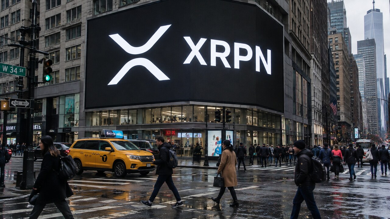 Groot reclamescherm op een straathoek in Manhattan met het XRP-logo en de letters XRPN, met voetgangers op straat