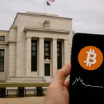Hand met smartphone met een Bitcoin-koersgrafiek voor het gebouw van de Federal Reserve in Washington