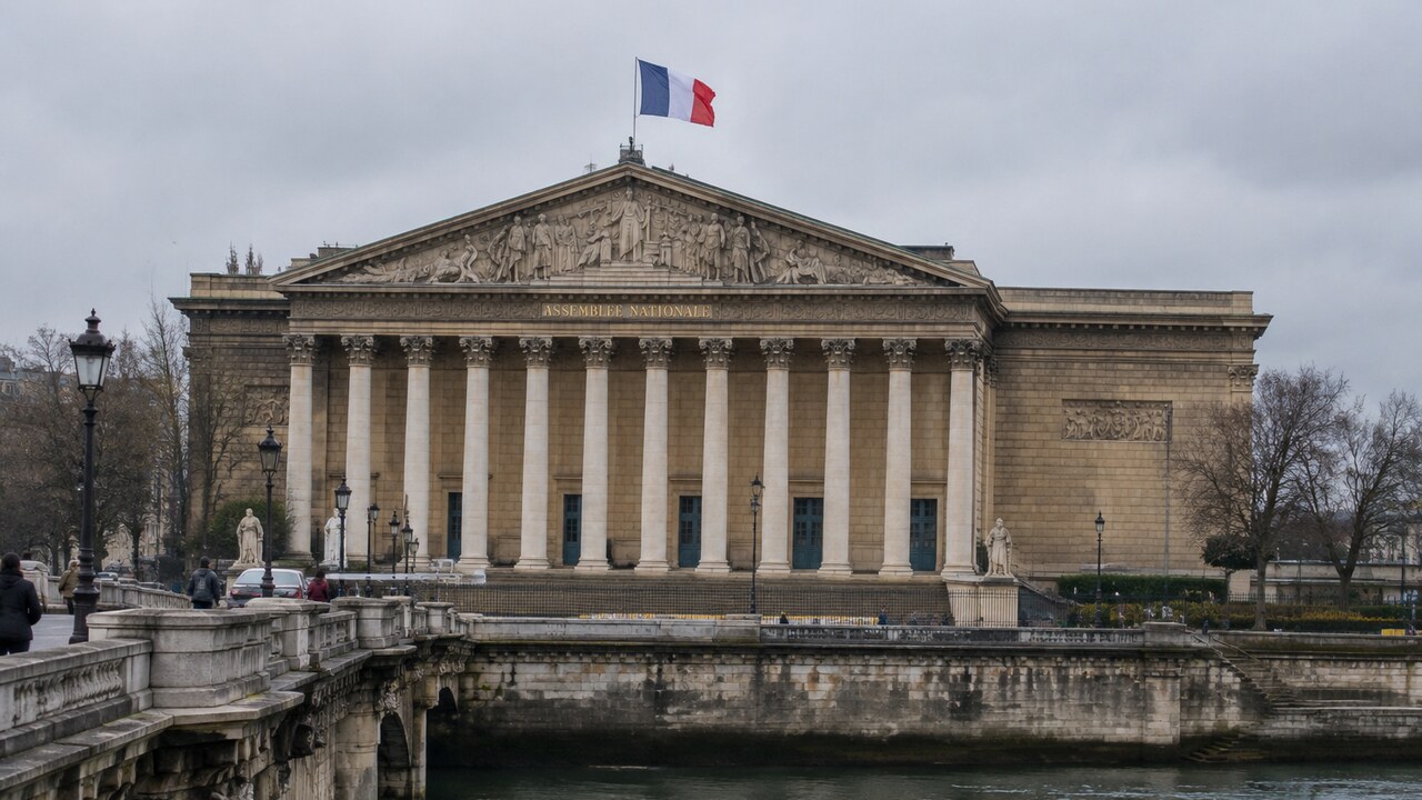 De Franse vlag wappert boven het Palais Bourbon, zetel van de Assemblée nationale in Parijs, op een bewolkte middag