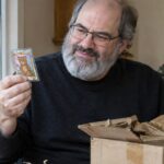 David Schwartz pakt aan een keukentafel een anoniem pakket uit en houdt een glimmende verzamelkaart met een teddybeer omhoog