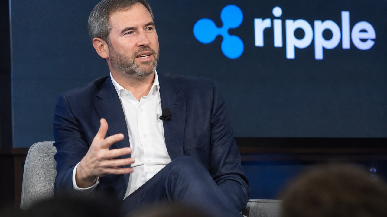 Ripple-CEO Brad Garlinghouse spreekt op een podium met een groot Ripple-logo op het scherm achter hem