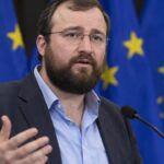 Cardano-oprichter Charles Hoskinson spreekt op een podium met Europese vlaggen op de achtergrond