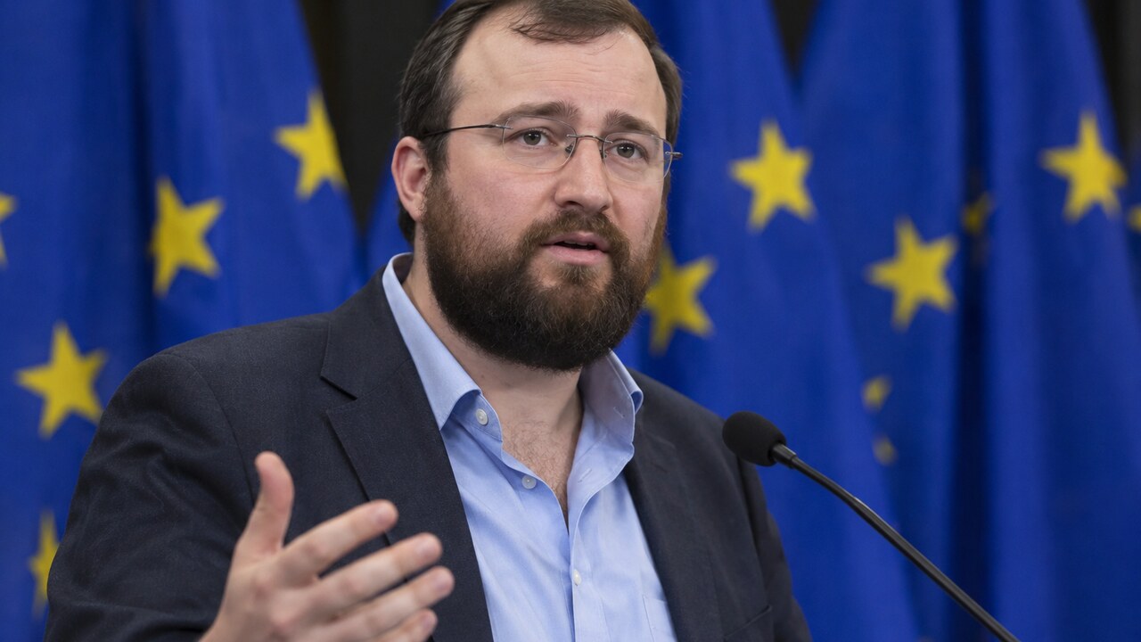 Cardano-oprichter Charles Hoskinson spreekt op een podium met Europese vlaggen op de achtergrond