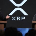 Twee sprekers in debat op een podium van een blockchainconferentie voor een groot scherm met het XRP-logo