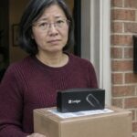 Vrouw in een deuropening houdt een ongeopend pakket met een Ledger hardware wallet vast en kijkt bezorgd