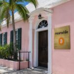 Roze koloniaal pand in Hamilton, Bermuda, met een messing naambord van Meanwhile en een oranje Bitcoin-symbool naast de voordeur