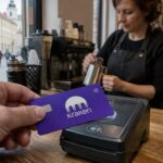 Hand houdt een paarse betaalkaart met Kraken-logo tegen een betaalterminal in een café in Vilnius