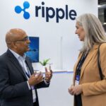 Stand met een groot Ripple-logo op een fintechbeurs, met twee bezoekers in gesprek op de voorgrond