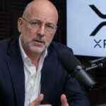 Man met bril spreekt in een podcaststudio in een microfoon, met het XRP-logo op een scherm achter hem